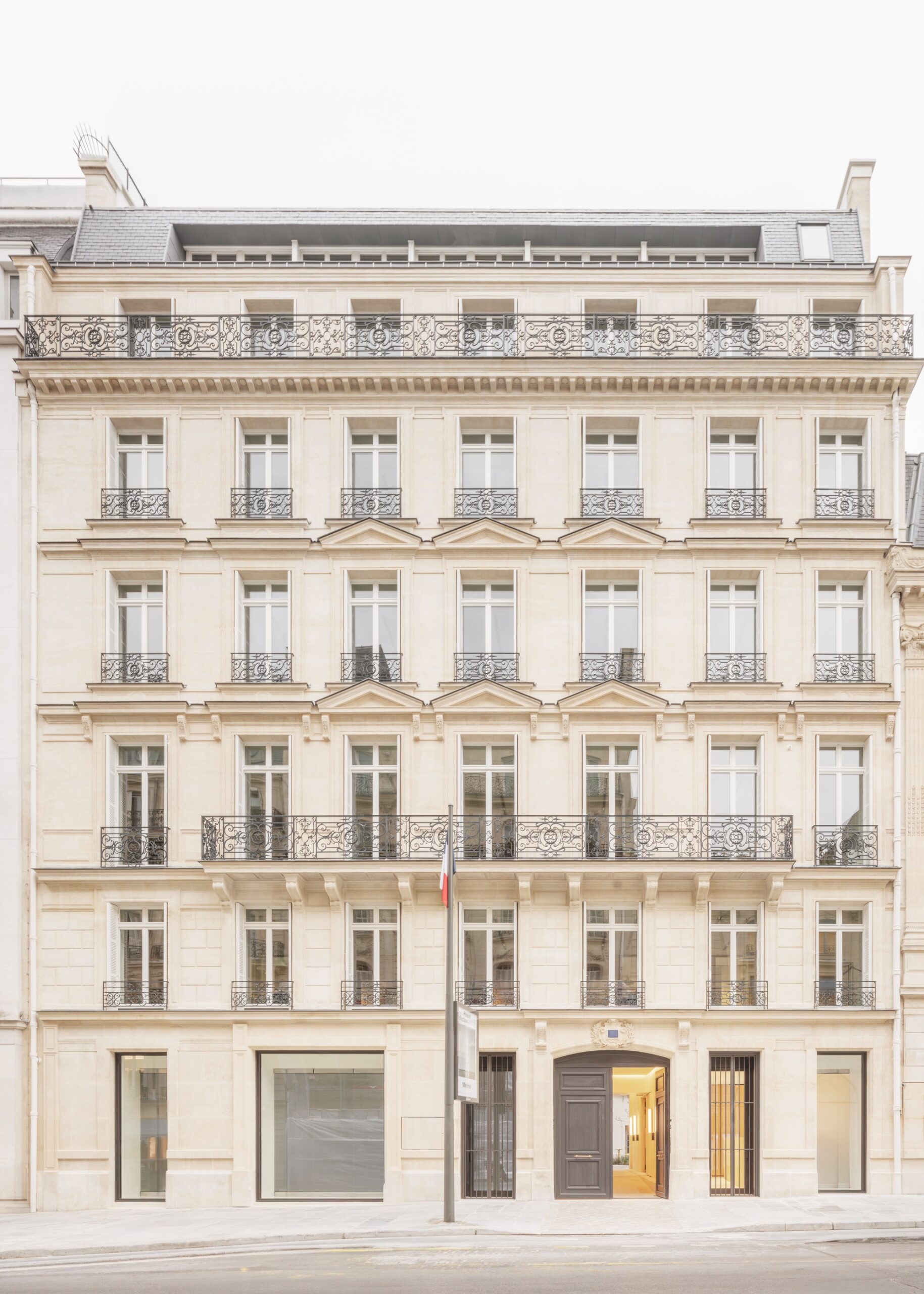 A full-view shot of a classic Haussmannian historic building facade in Paris, featuring ornate iron balconies and limestone walls, restored by Barthélémy Griño.