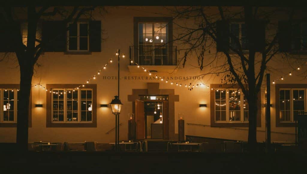Exterior night view of Landgasthof Riehen hotel showing the historic facade illuminated by warm string lights and traditional lanterns.