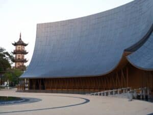 Low angle shot of the curved grey facade of the Zhouzhuang theatre against a clear sky with a pagoda visible.