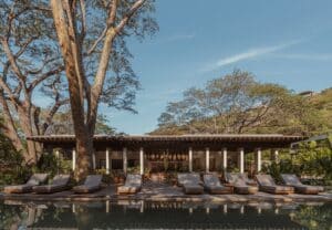Front view of the Andaz Beach Club pavilion with a reflective pool and lounge chairs under a clear blue sky.