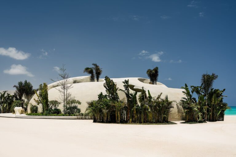External view of ESCA Playa’s white dome-like structures surrounded by tropical greenery and white sand.