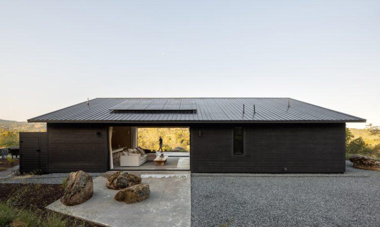 Exterior view of Casa Roca's black timber facade with large sliding glass doors and natural boulders integrated into the concrete patio.