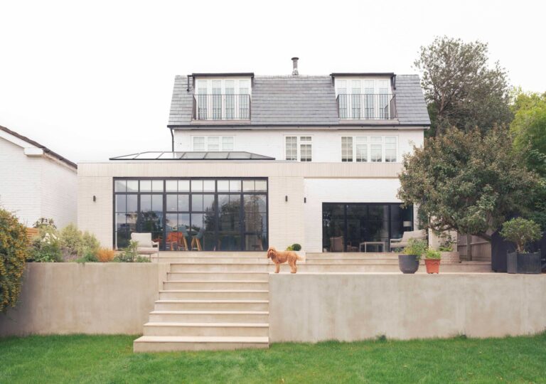Rear elevation of Wimbledon House showing a modern white brick extension with large black-framed Crittall-style windows and a tiered stone terrace.