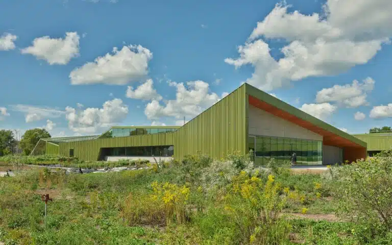 Daylight exterior of Thaden School showing the green metal cladding and large glass windows integrated with wild landscape and gardens.