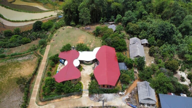 Drone perspective looking directly down at the red and white butterfly roofs of Hangtao School, surrounded by lush green forests.