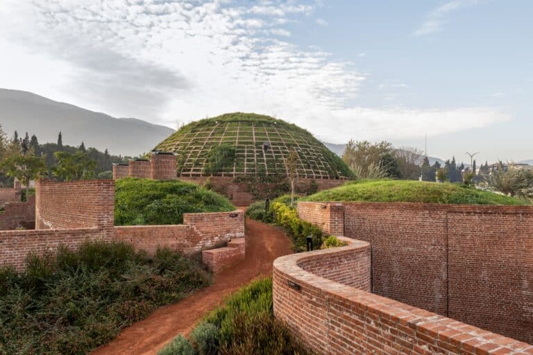 Curving brick walls and red earth pathways leading toward the central green dome.