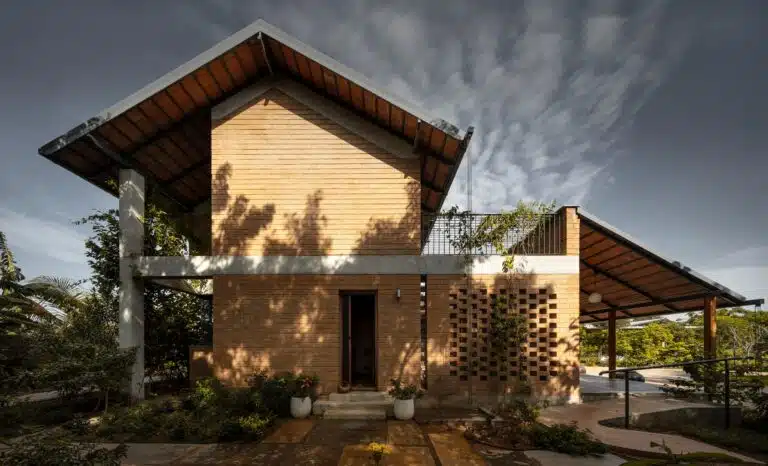 Nandivardhana house nestled in a tranquil agricultural landscape, showing the integration of brick architecture with surrounding fields and greenery.