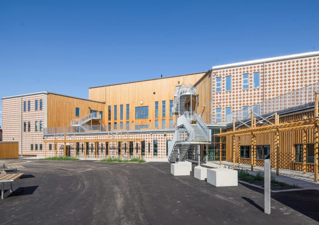 Main entrance courtyard of &Auml;ngsdal School featuring a sculptural metal staircase and decorative diamond-patterned concrete walls.