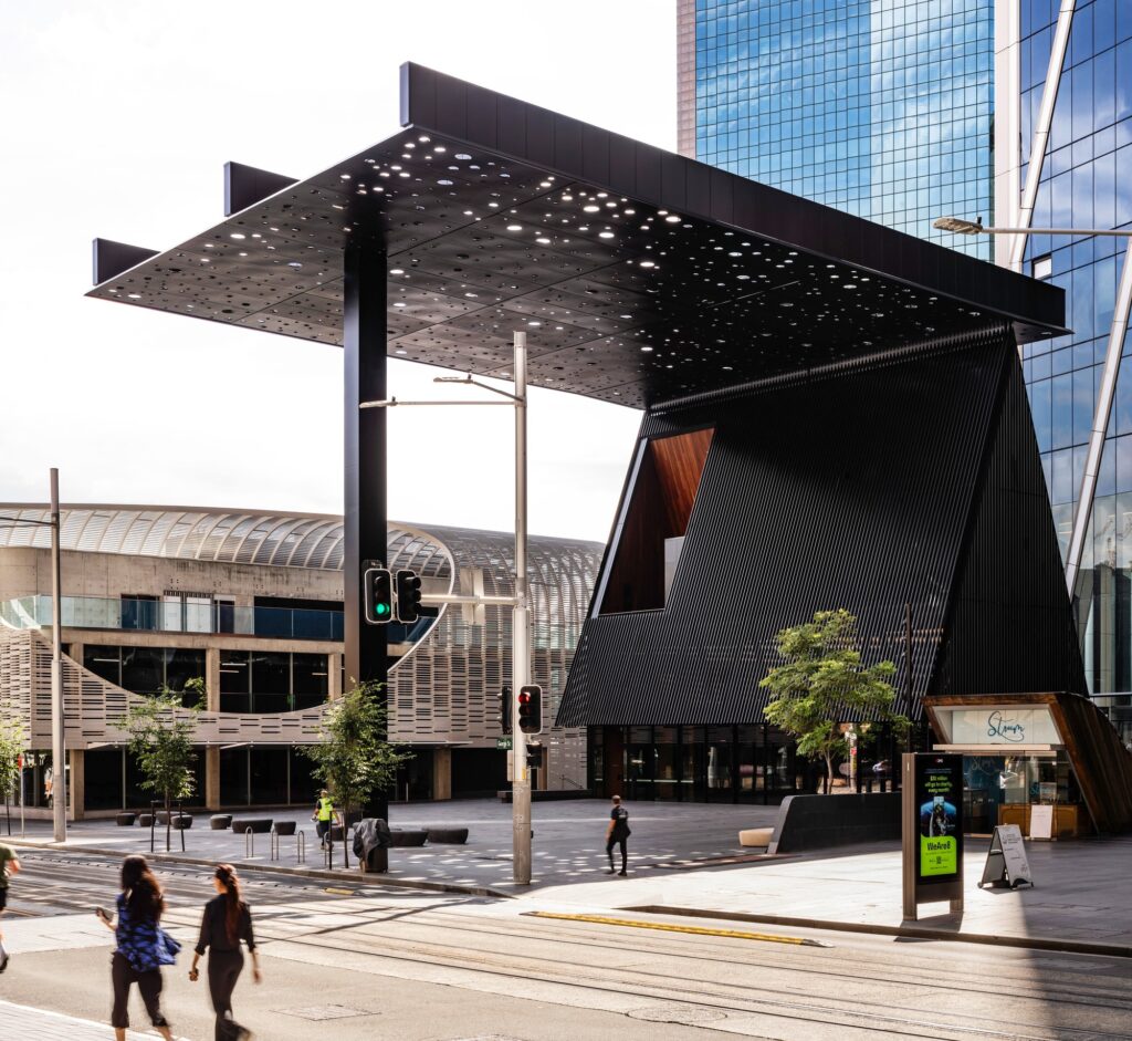 Exterior view of George Street Community Building designed by Adjaye Associates, featuring the distinctive 27x34m perforated art canopy by Daniel Boyd and the plaza beneath it.