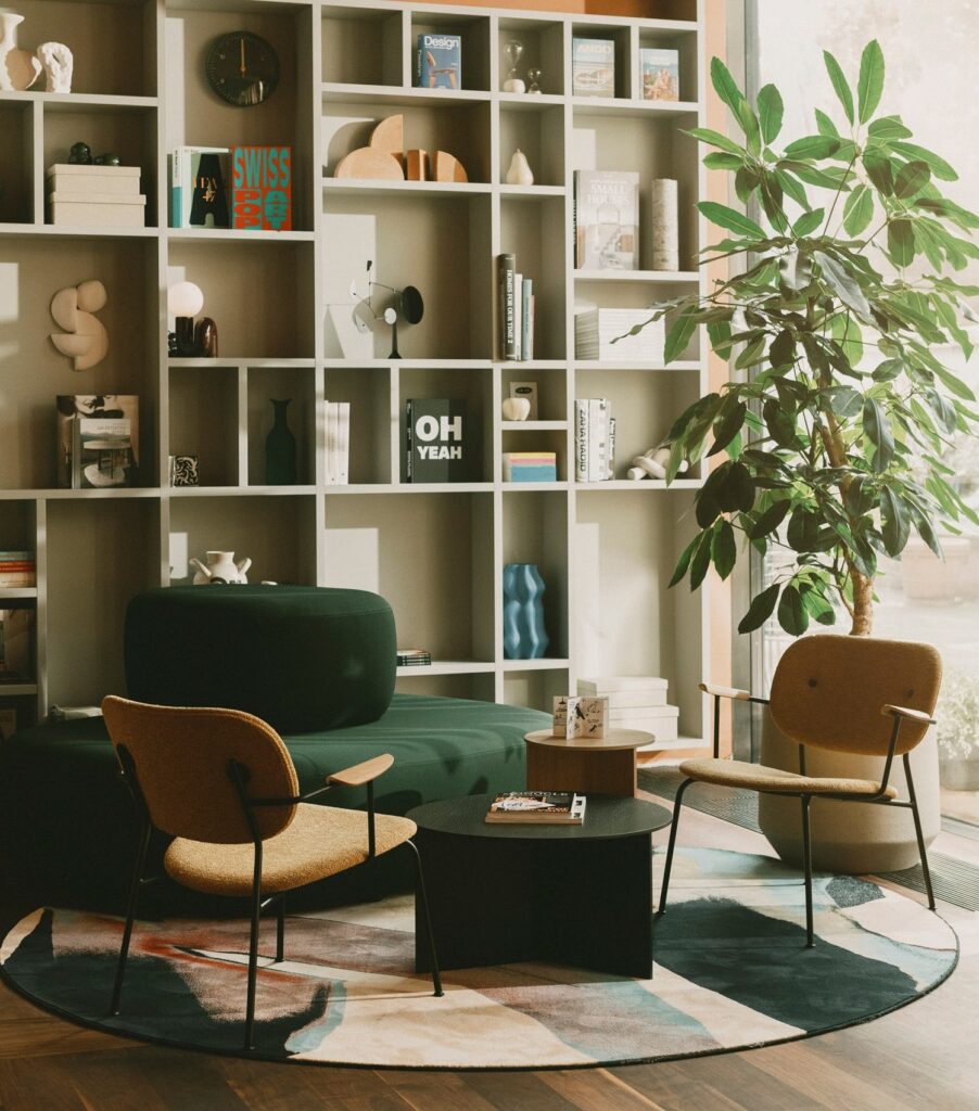 Stylish hotel lobby lounge with a large minimalist bookshelf, green velvet seating, and designer armchairs on a geometric rug.