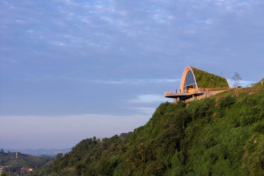 Side profile of the Pujiang Platform on a steep green hill, showing the arched structure covered in vegetation.