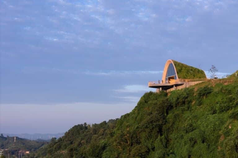 Side profile of the Pujiang Platform on a steep green hill, showing the arched structure covered in vegetation.