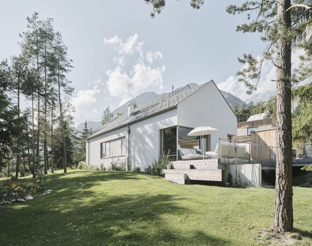 Wide angle exterior of a minimalist house with a large green lawn and mountains in the background.