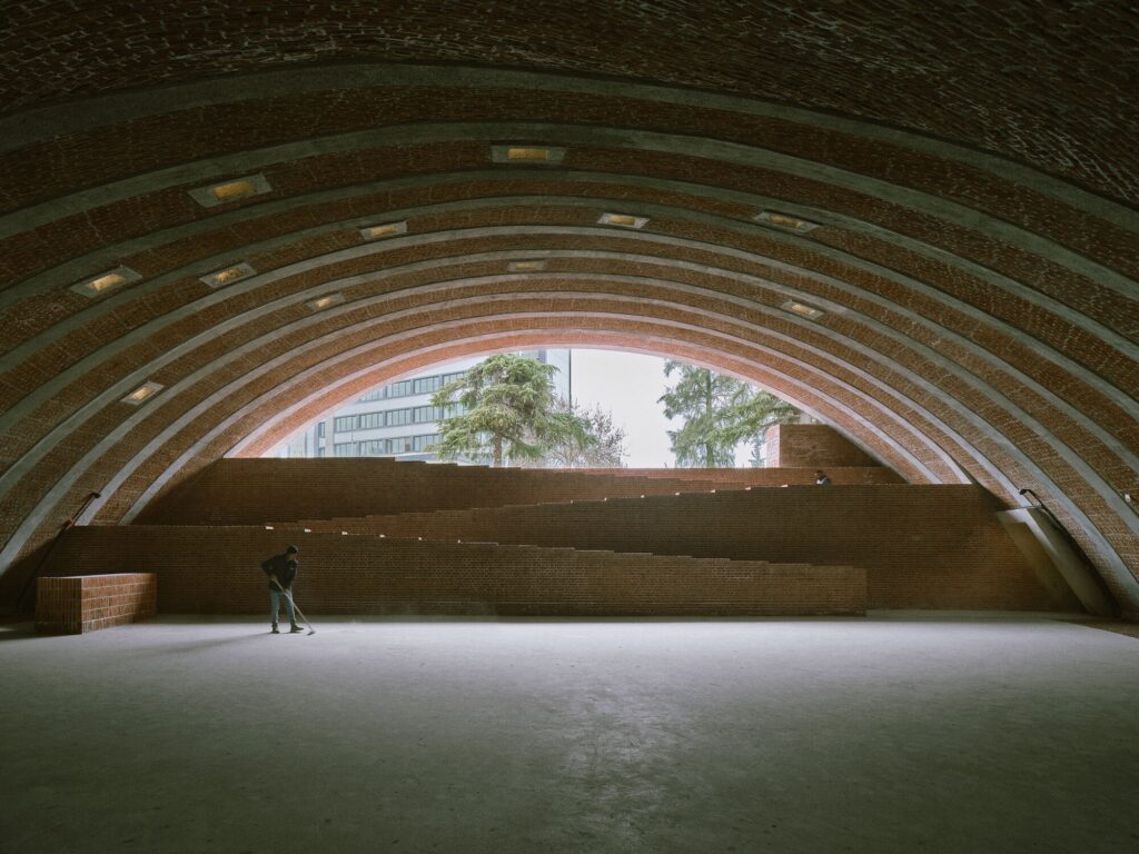 Wide interior space under a massive ribbed concrete arch with tiered brick seating.