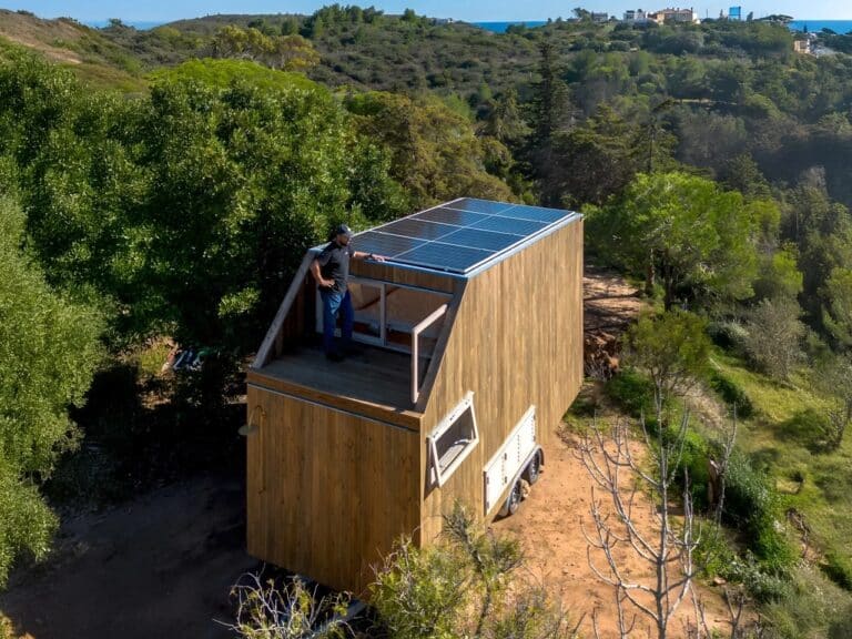 Aerial view of Duna Tiny House showing rooftop solar panels and a wooden deck in a natural landscape.