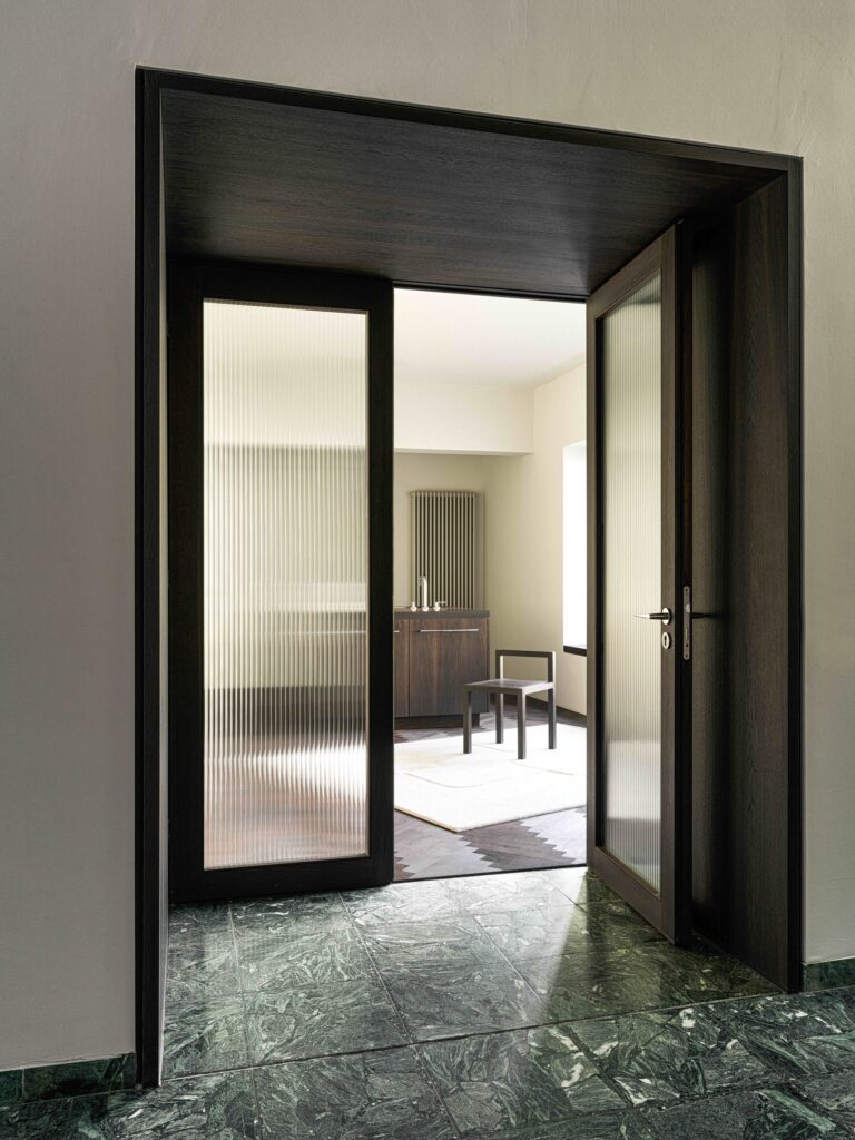 Interior doorway looking from a green marble floor into a bright kitchen area with fluted glass doors.