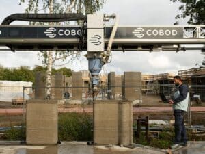 A COBOD BOD2 3D construction printer creating the concrete walls of the Skovsporet student housing project with a technician monitoring progress.