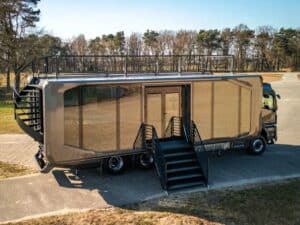 Wide shot of the Shiver x Expandable unit fully deployed with a spiral staircase and rooftop railing in a forest clearing.