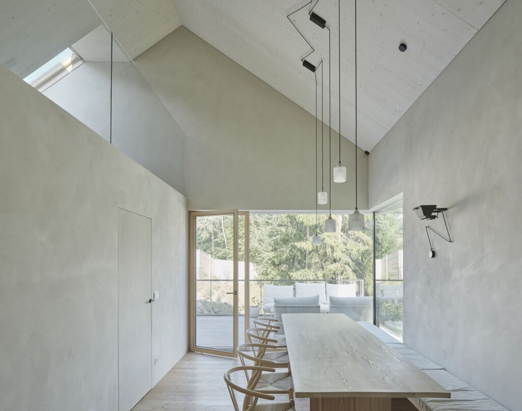 Dining area with a long wooden table and bench seating, featuring a large window overlooking a forest in House Am Feuerbachl.