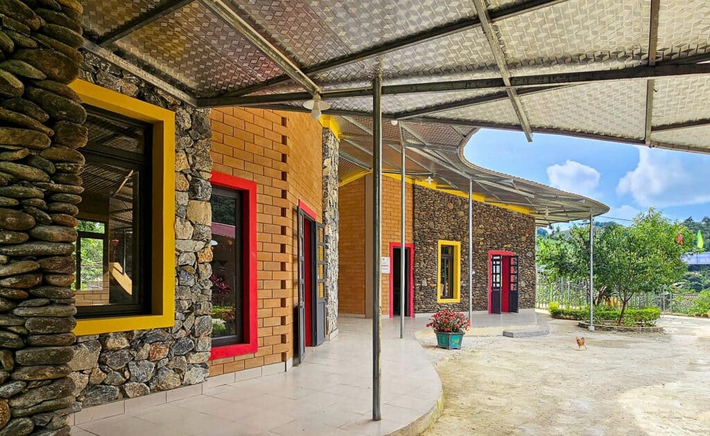 Architectural detail of the school exterior featuring textured stone walls, yellow and red window frames, and a curved covered walkway.