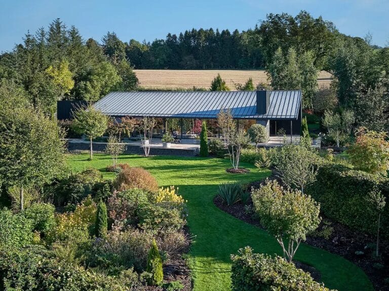 Wide aerial view of Grianan house in the Scottish countryside featuring a dark metal pitched roof surrounded by lush green landscaped gardens.