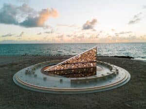 Aerial view of Nahnu Library, a triangular glass structure filled with books on a circular platform at Miami Beach during sunset.