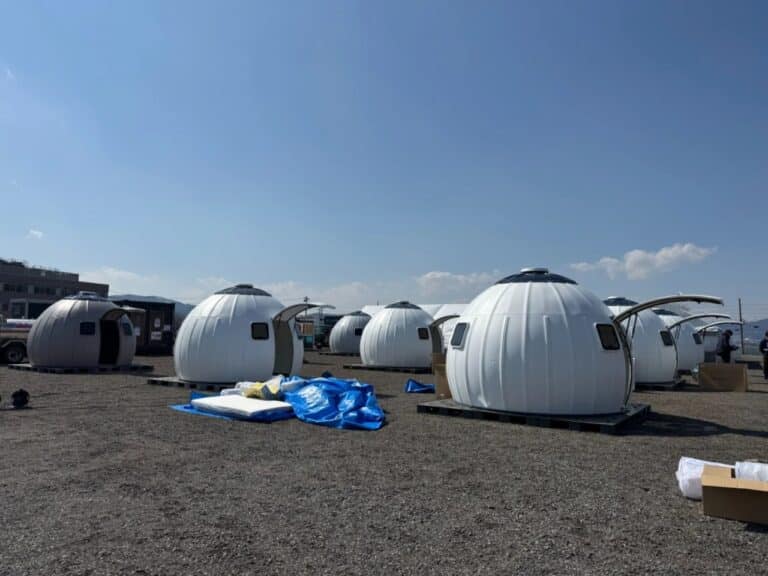 A row of white Ezdome disaster relief pods installed on a gravel site under a clear blue sky.