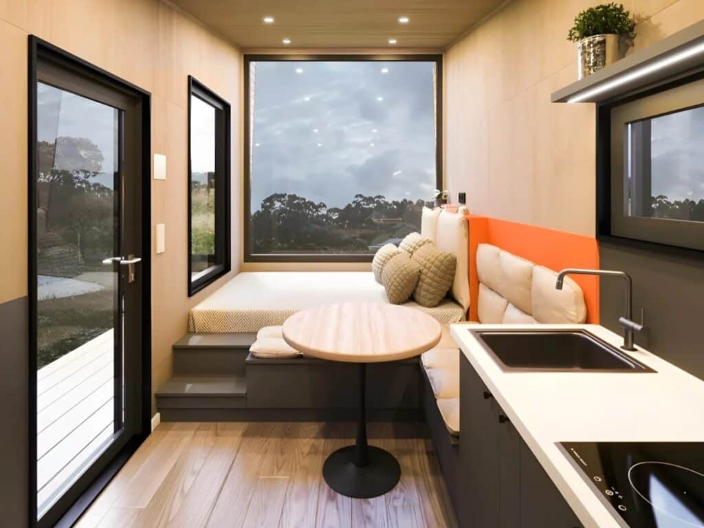 Interior of Ambra House showing a multifunctional living area with a bed by a large window, a dining table, and a compact kitchen unit.