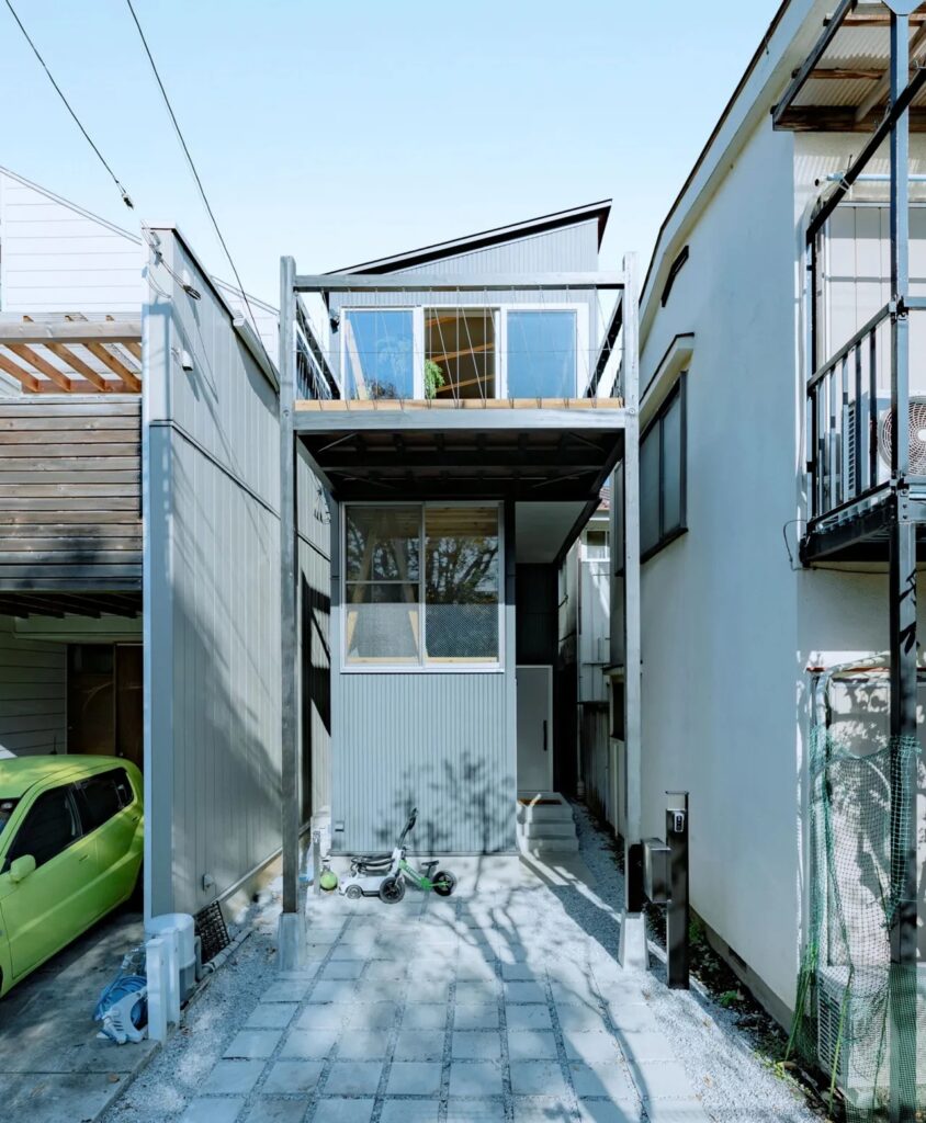 Street view of the narrow Fukasawa House, showcasing the cantilevered upper floor and a small parking area on a tight urban plot.
