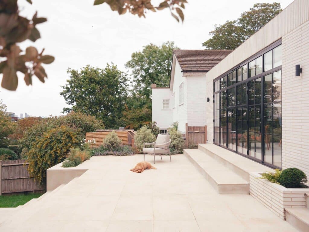 A spacious outdoor stone terrace at Wimbledon House with a contemporary lounge chair and views of the lush green backyard.