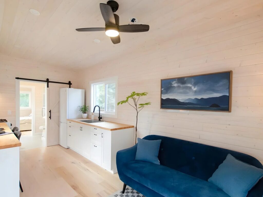 Interior view of Barred Owl tiny house showing a blue velvet sofa, white kitchen cabinets, and light wood walls.