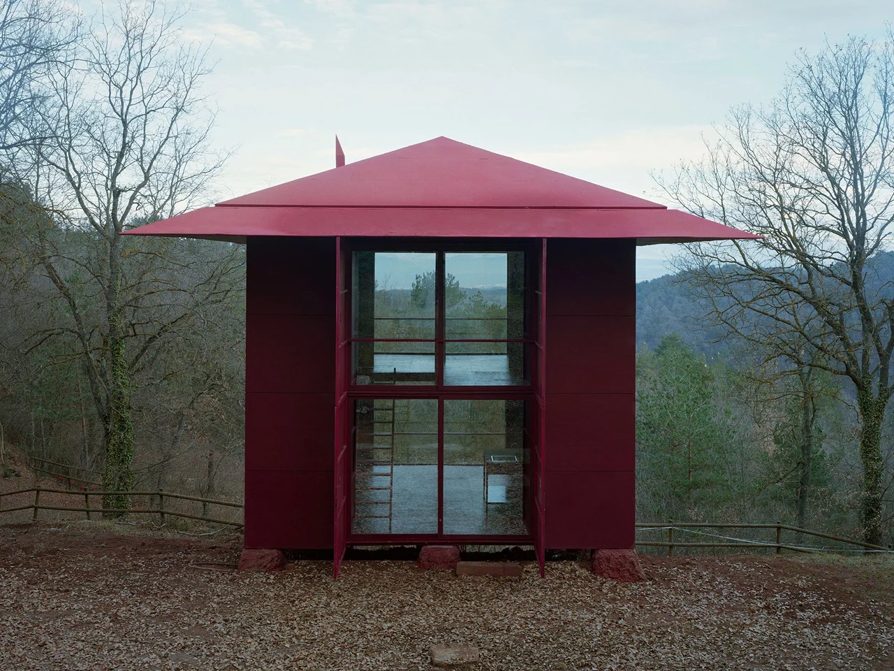 Prefab Changeover house closed facade showing modular red panels and wide eaves in a natural woodland setting.