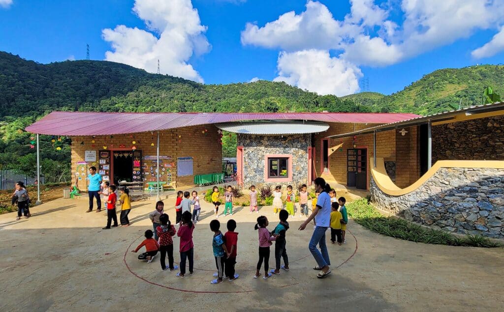 A group of students gathered in a circle for activities in the main courtyard under a bright sky with mountains in the background.