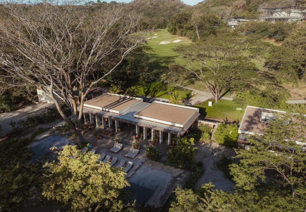 High-angle view of the beach club buildings situated between a golf course and a lush tropical forest.