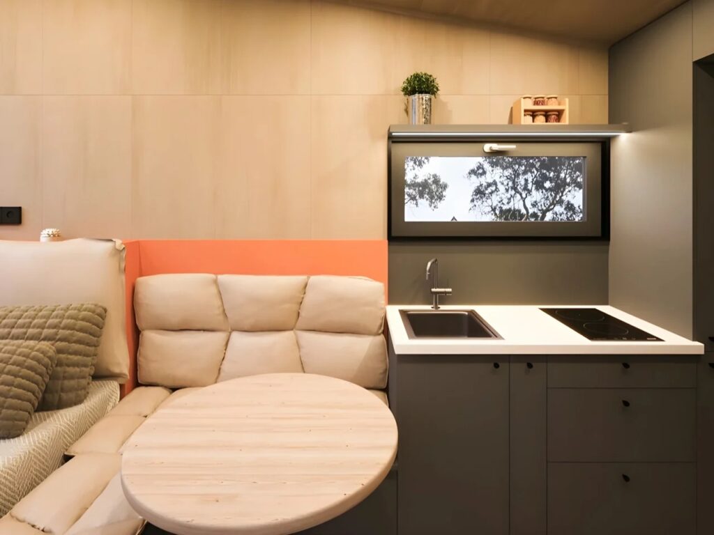 Minimalist kitchen and dining corner in Ambra House with dark grey cabinetry, integrated sink, and a circular light wood table.