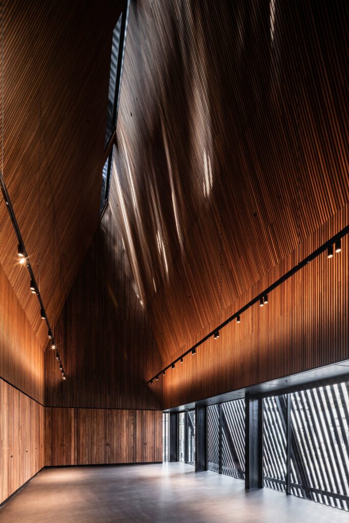 Interior view of the George Street Community Building hall, featuring high, slatted timber walls and ceiling, with beams of filtered sunlight creating a dramatic effect.
