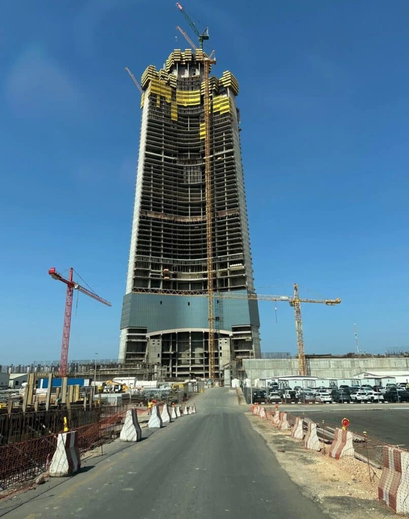 JEC Tower in Jeddah under construction, showcasing its central core, mixed-use spaces including offices, hotel, residential units, and engineering challenges as it rises above 1 kilometer, providing insight into modern skyscraper design and construction techniques