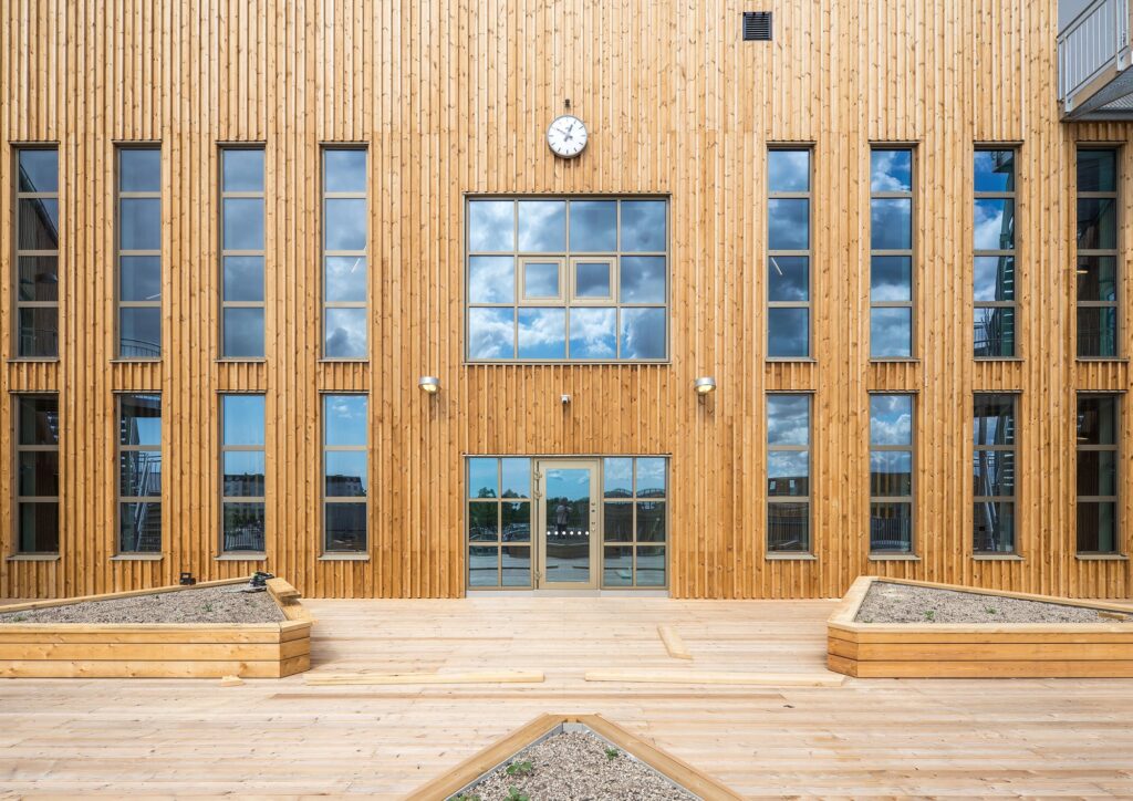 Symmetrical view of the wooden vertical cladding facade at &Auml;ngsdal School with large glass windows and outdoor seating planters.