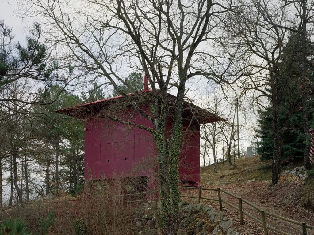 Interior view of the Prefab Changeover house showing red monolithic walls, plywood panels, and a structural column.