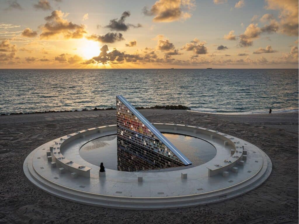 Wide angle shot of a person sitting on the circular bench of Nahnu Library facing the ocean at sunset.