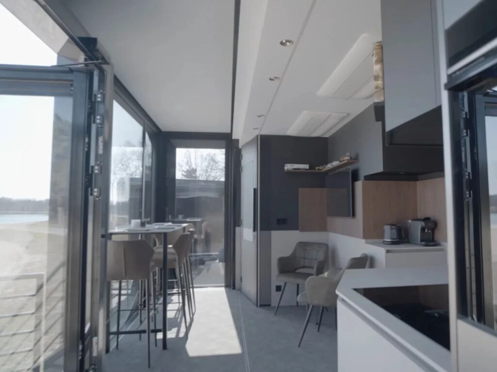 Interior view of the Shiver x Expandable living room and dining area overlooking a lake through large windows.