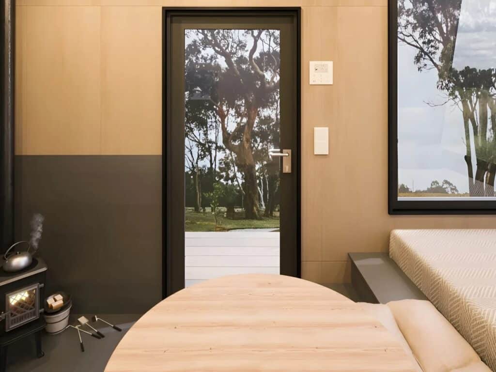 View of the entrance door from inside Ambra House, looking out onto a wooden deck and lush green trees.