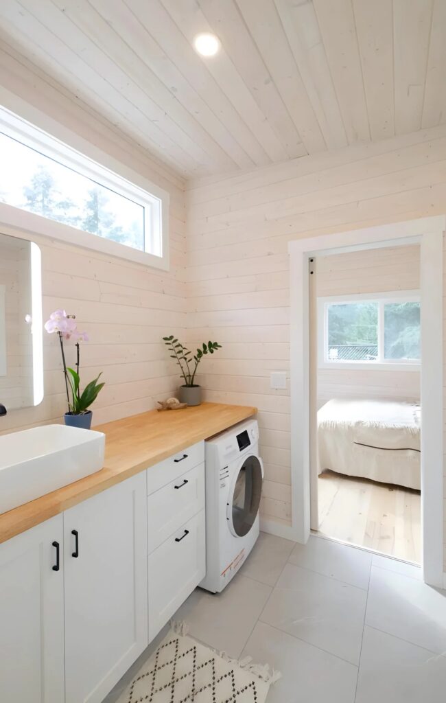 Integrated laundry area in a tiny house bathroom with a white washing machine and vessel sink.
