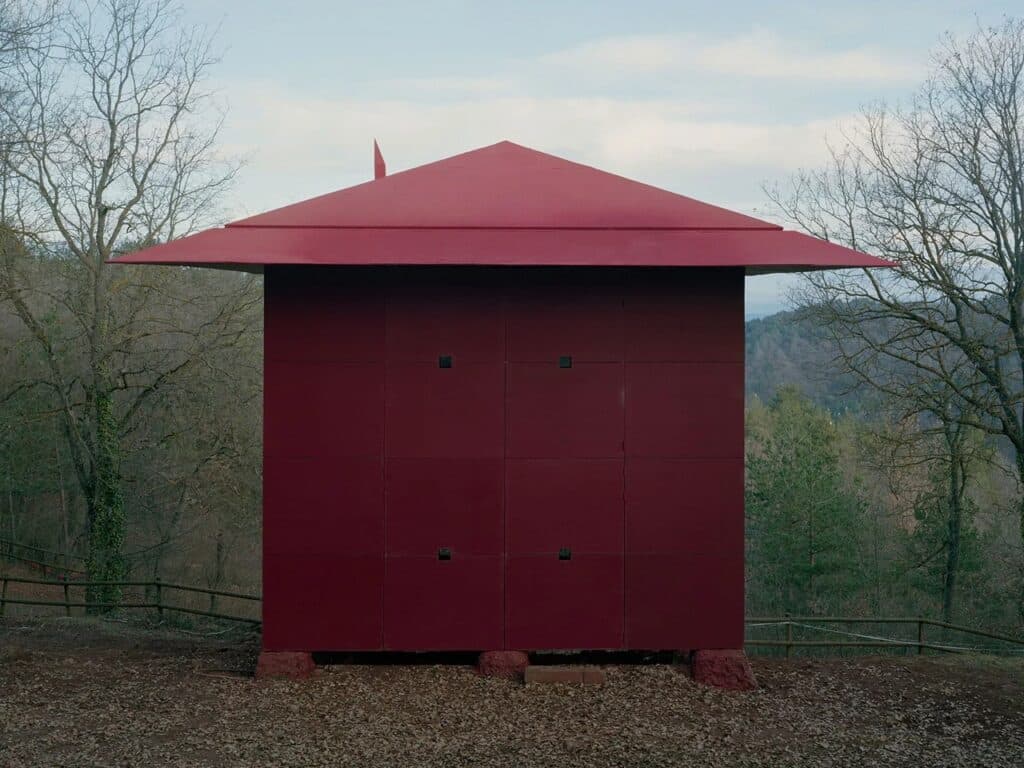 Wide landscape shot of the Prefab Changeover house nestled deep within a lush, temperate forest on a hillside.