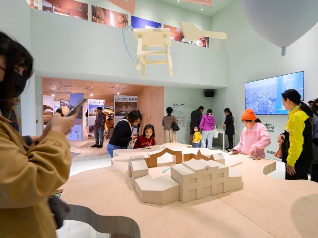 Close-up of children exploring a white architectural model placed on a light wood table within the pavilion's exhibition area.