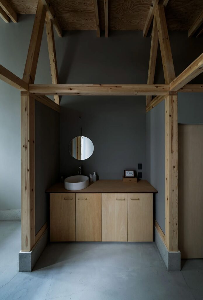 Minimalist bathroom vanity area in Fukasawa House, featuring a round mirror, wooden cabinetry, and exposed timber pillars.