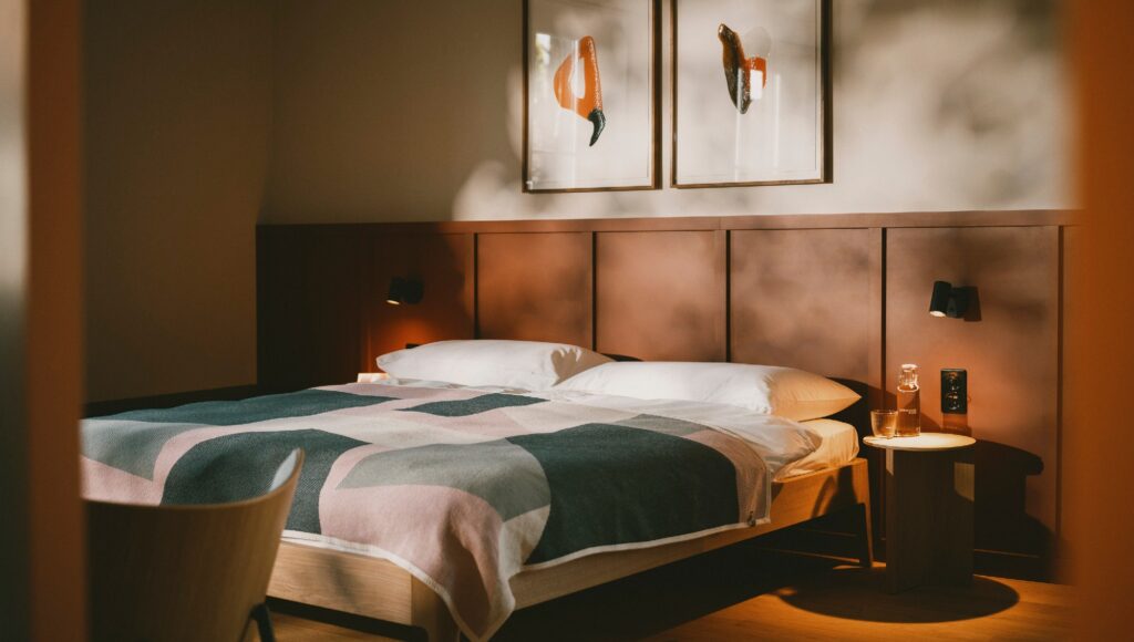 Minimalist hotel bedroom at Landgasthof Riehen with wood paneling, a colorful patterned throw, and warm bedside lighting.