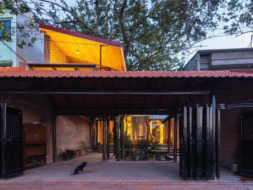 Nang House in Hanoi suburbs blending contemporary architecture with traditional elements, showcasing brick and wood materials, integrated gardens, and open spaces that connect family living with the natural environment.