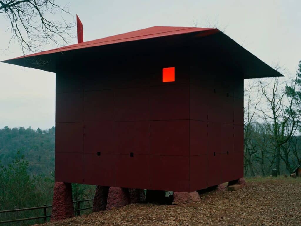 Close-up view of the unique red, textured concrete-like pillars supporting the elevated Prefab Changeover house structure.