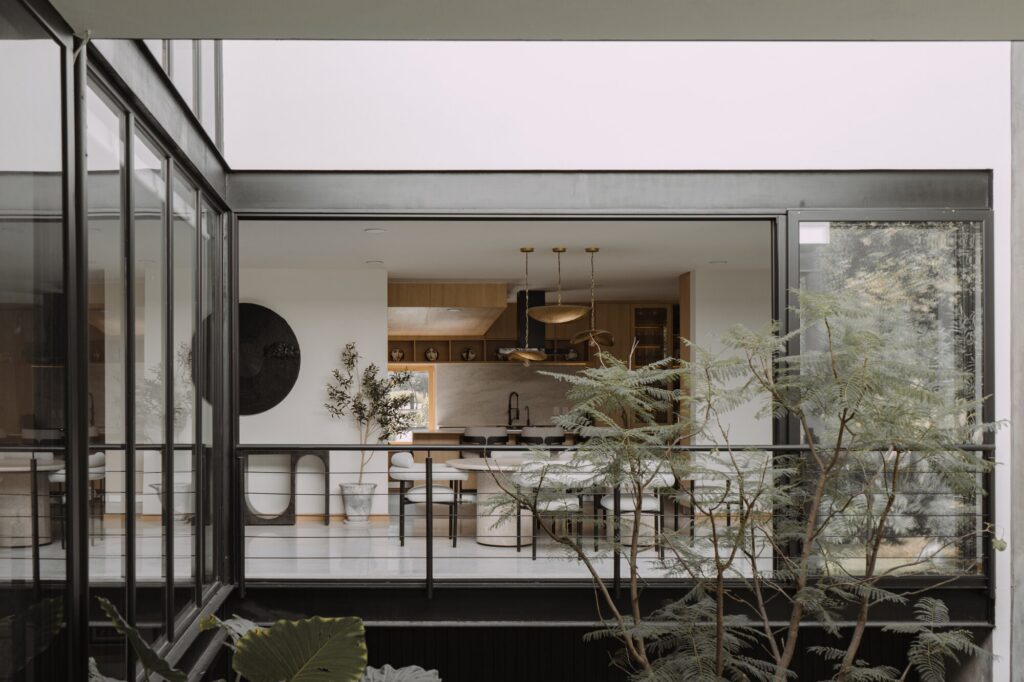 Casa EV residential design in Guadalajara featuring innovative integration of privacy, natural light, wooden materials, interconnected living spaces, central staircase, and landscaped exterior blending indoor and outdoor experiences.